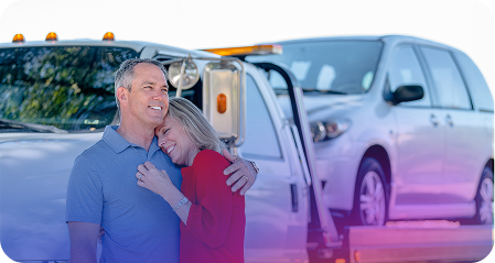 A man holding his wife, front of a tow truck towing their donated car